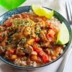a bowl of beef stew with cous cous ad lime wedges