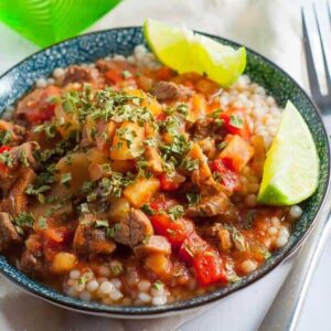 a bowl of beef stew with cous cous ad lime wedges