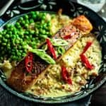 a bowl of cooked salmon in green curry sauce with chili, shallots and peas