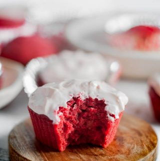 a single red velvet cupcake on a plate with a bite taken out