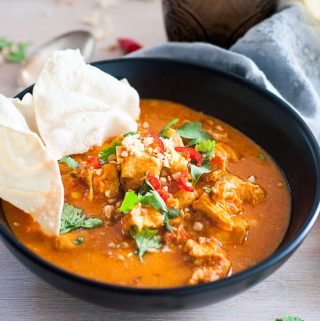 Pressure cooker chicken curry in a black bowl with pappadaum