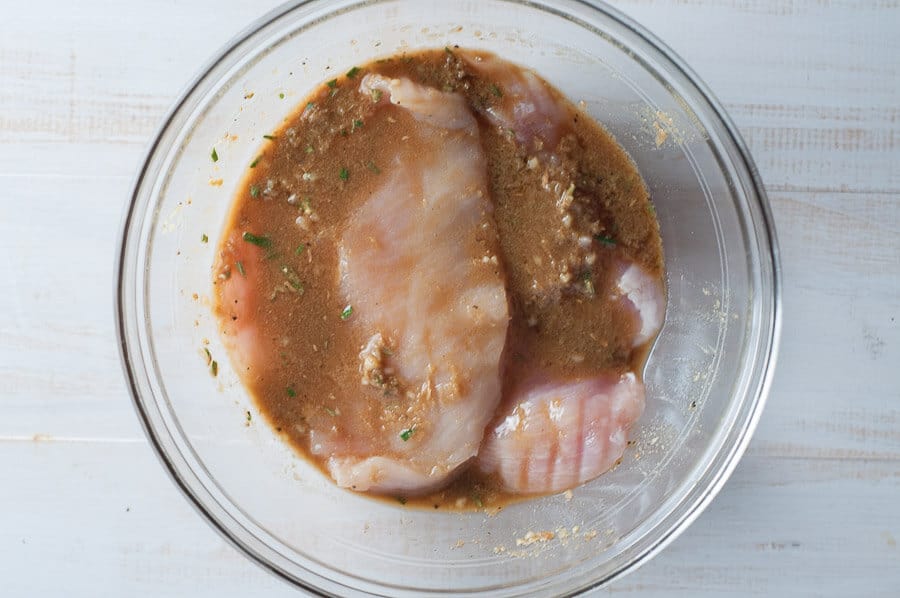 chicken marinating in a glass bowl