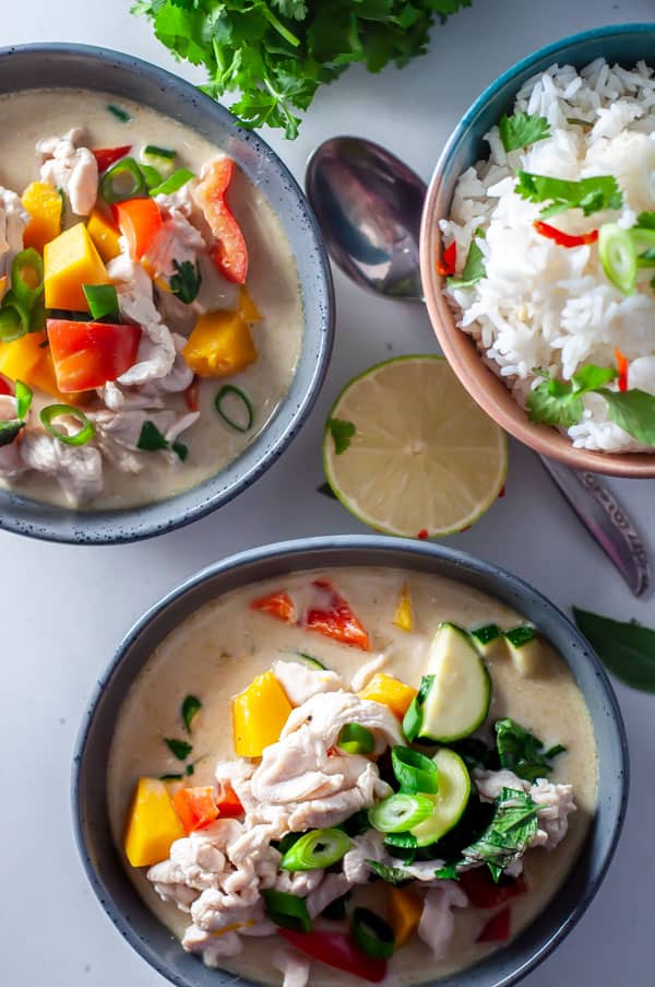 two bowls of thai green chicken curry with rice and lime