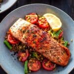 a piece of salmon on a bed of lentils with tomatoes, beans and lemon wedge