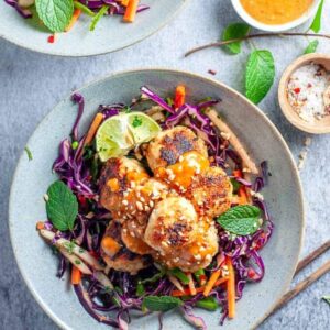 a plate of asian chicken meatballs on top of cabbage slaw