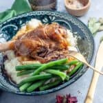 cooked lamb shank on top of potato with side of green beans