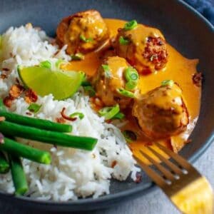 4 chicken meatballs with peanut sauce and rice in a bowl