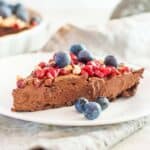 a slice of chocolate date tart on a white plate with blueberries