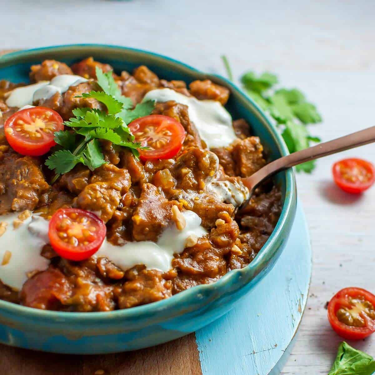 beef masala in a blue bowl with yoghurt and tomatoes