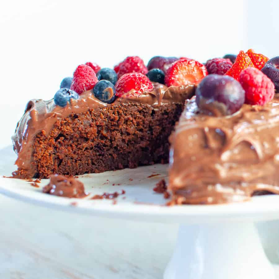 Chocolate date cake with berries on a white serving platter with a slice out