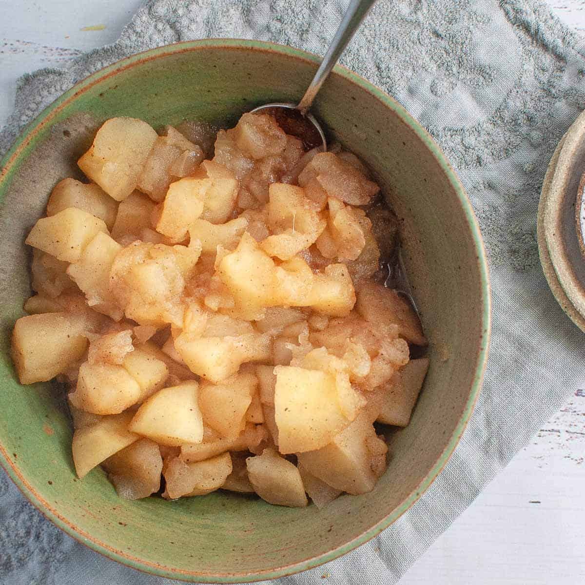 cooked stewed apples in a green bowl with a spoon ready to eat