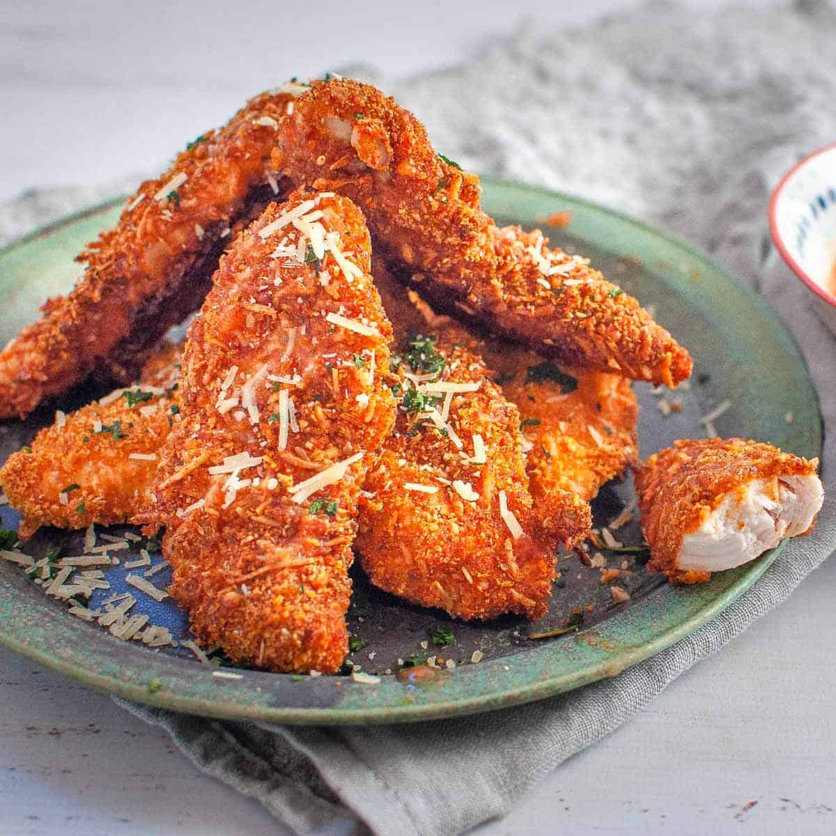 stacked chicken tenders on a plate with one that is half eaten