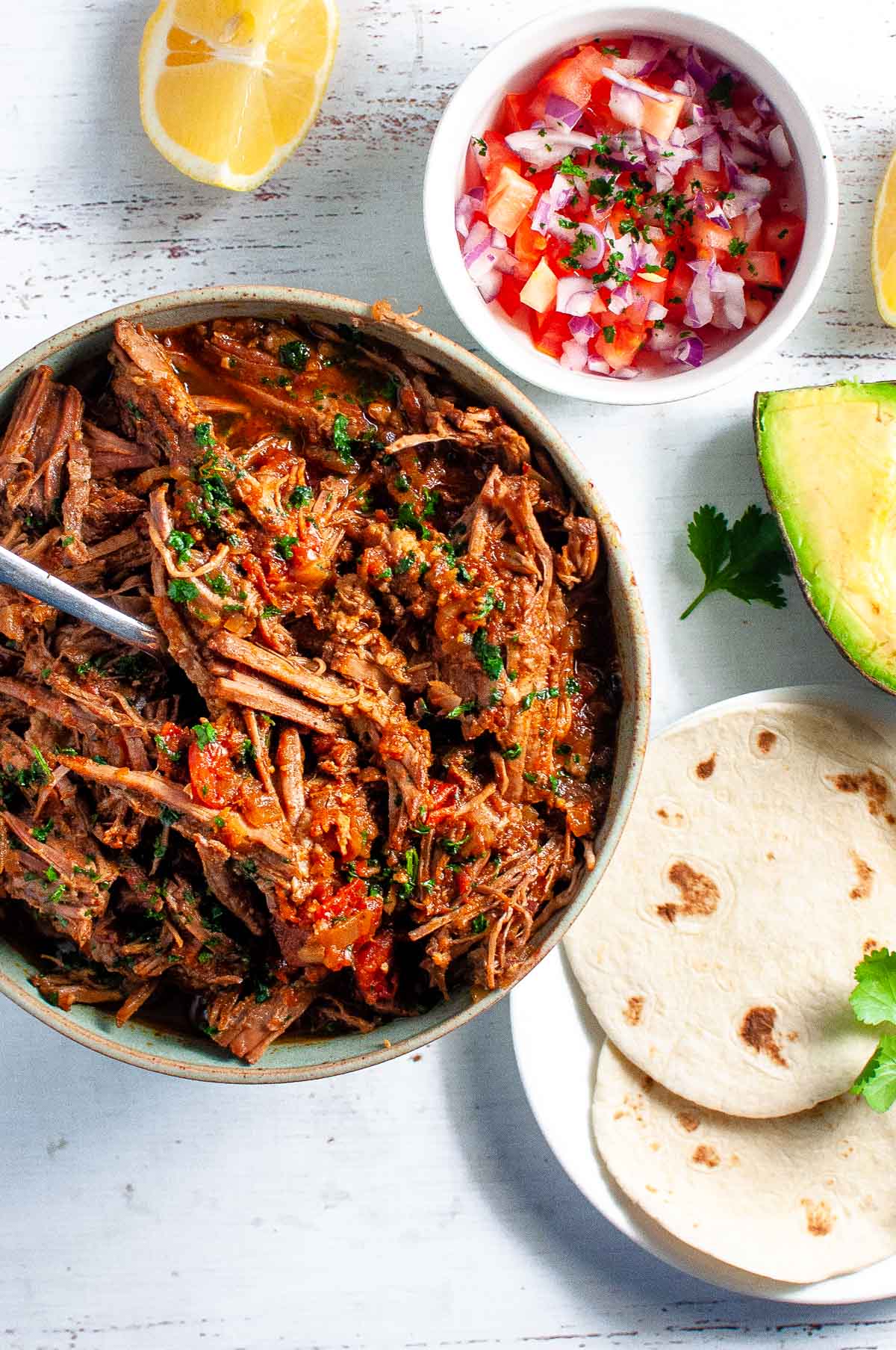 a bowl of shredded beef with soft tacos, salsa and avacado