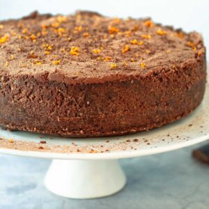 chocolate cheesecake with orange zest on top sitting on a cakestand