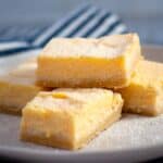 4 lemon bars stacked on a grey plate
