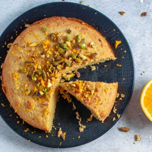 Orange polenta cake with a slice out on a black plate