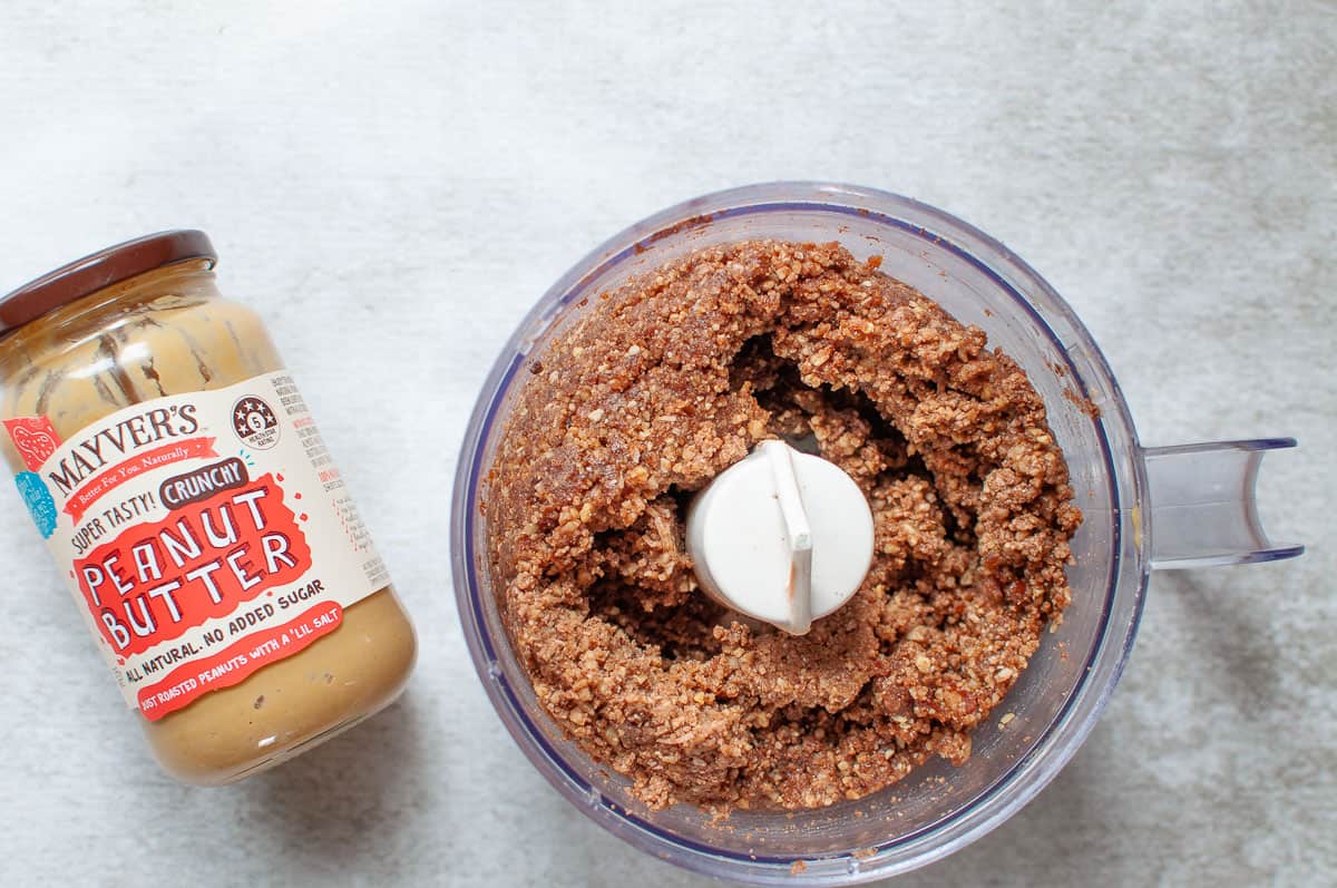 bliss ball mixture in a food processor beside a jar of peanut butter