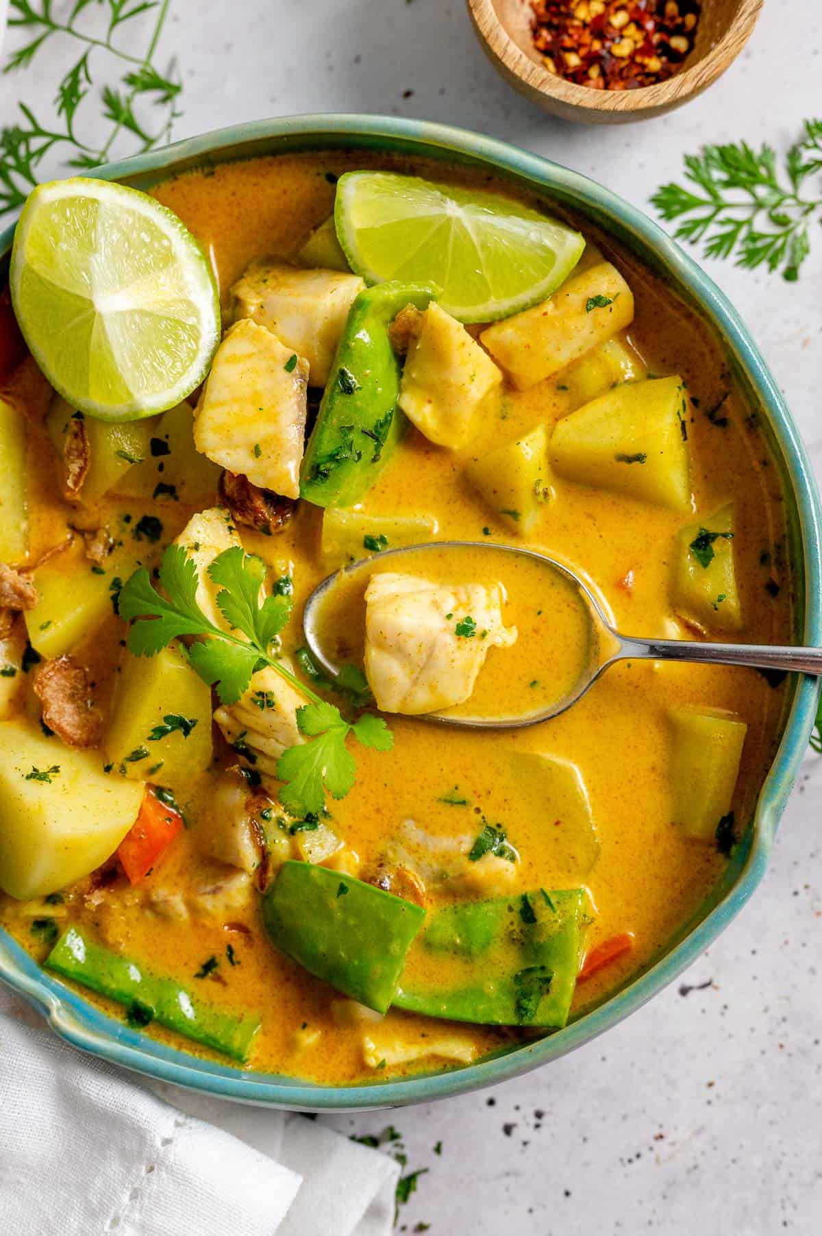 Yellow Fih curry in a blue bowl with a spoon and lime wedges