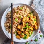 a white bowl with chilli chicken and rice and chopsticks