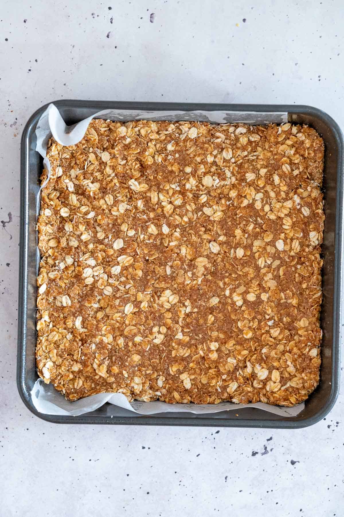 anzac slice in a square baking tin ready for baking