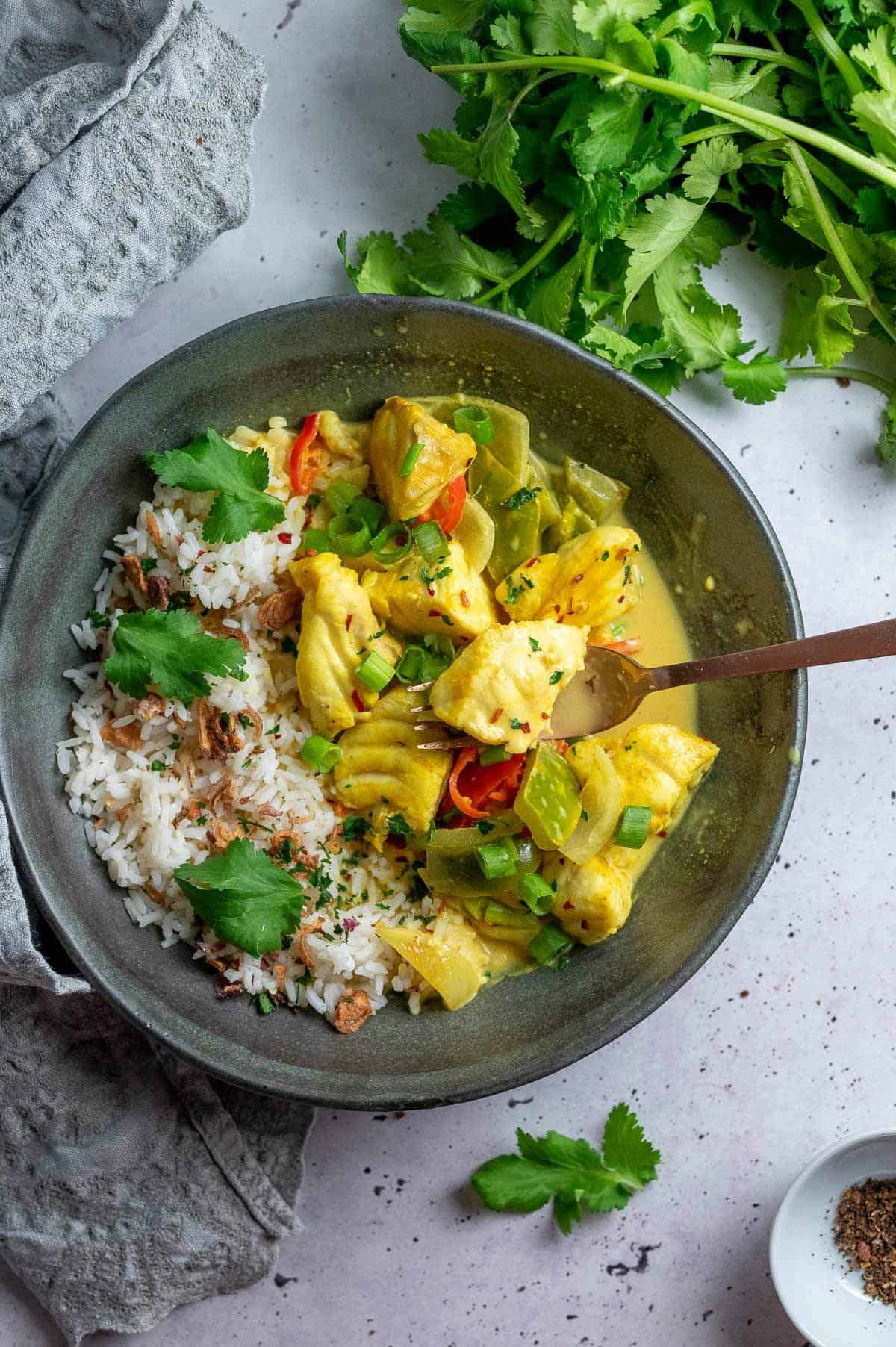 a bowl of kerala fish curry with a spoon in it and a piece of fish on spoon