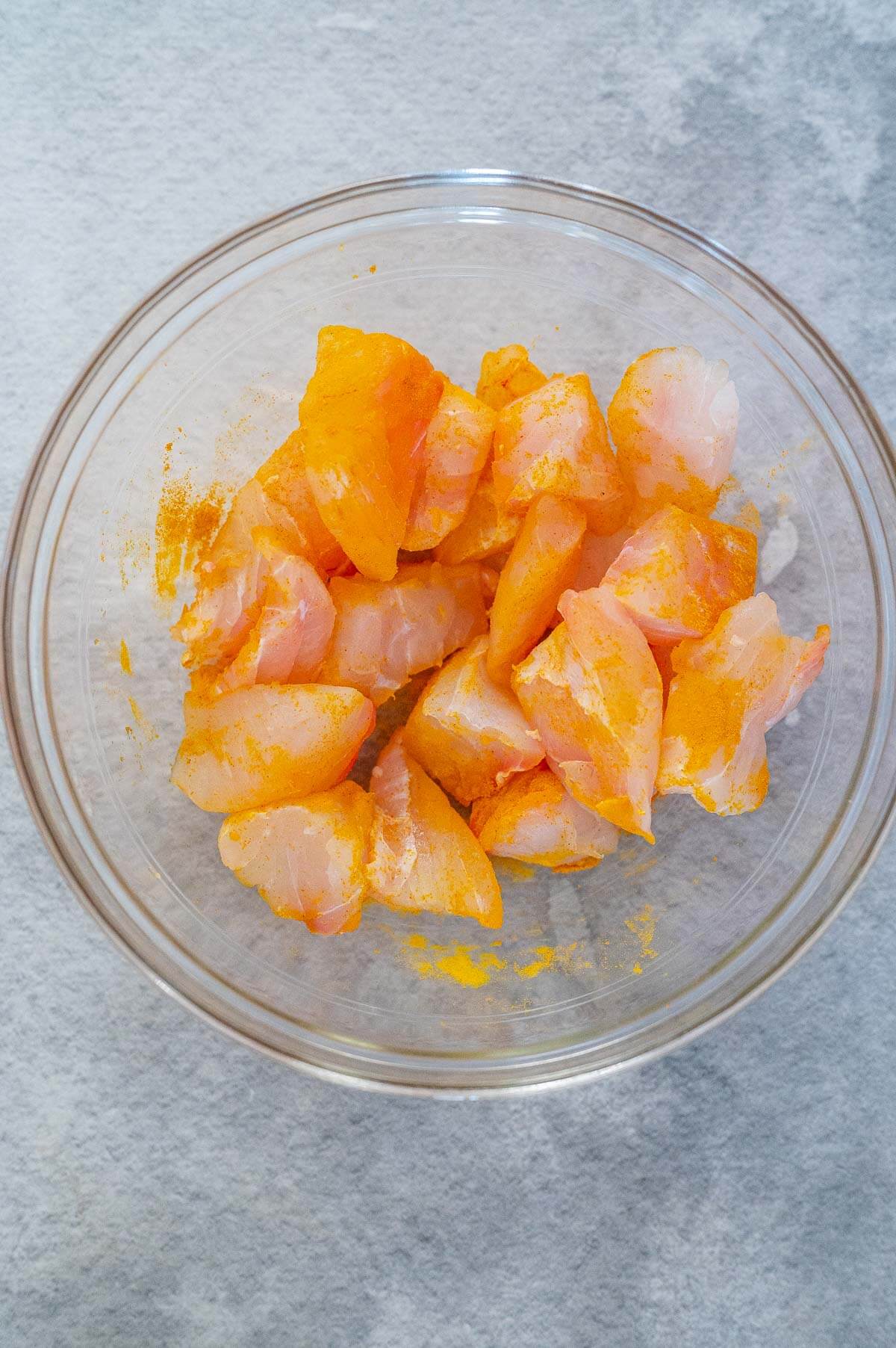 chopped fish coated in tumeric in a clear bowl