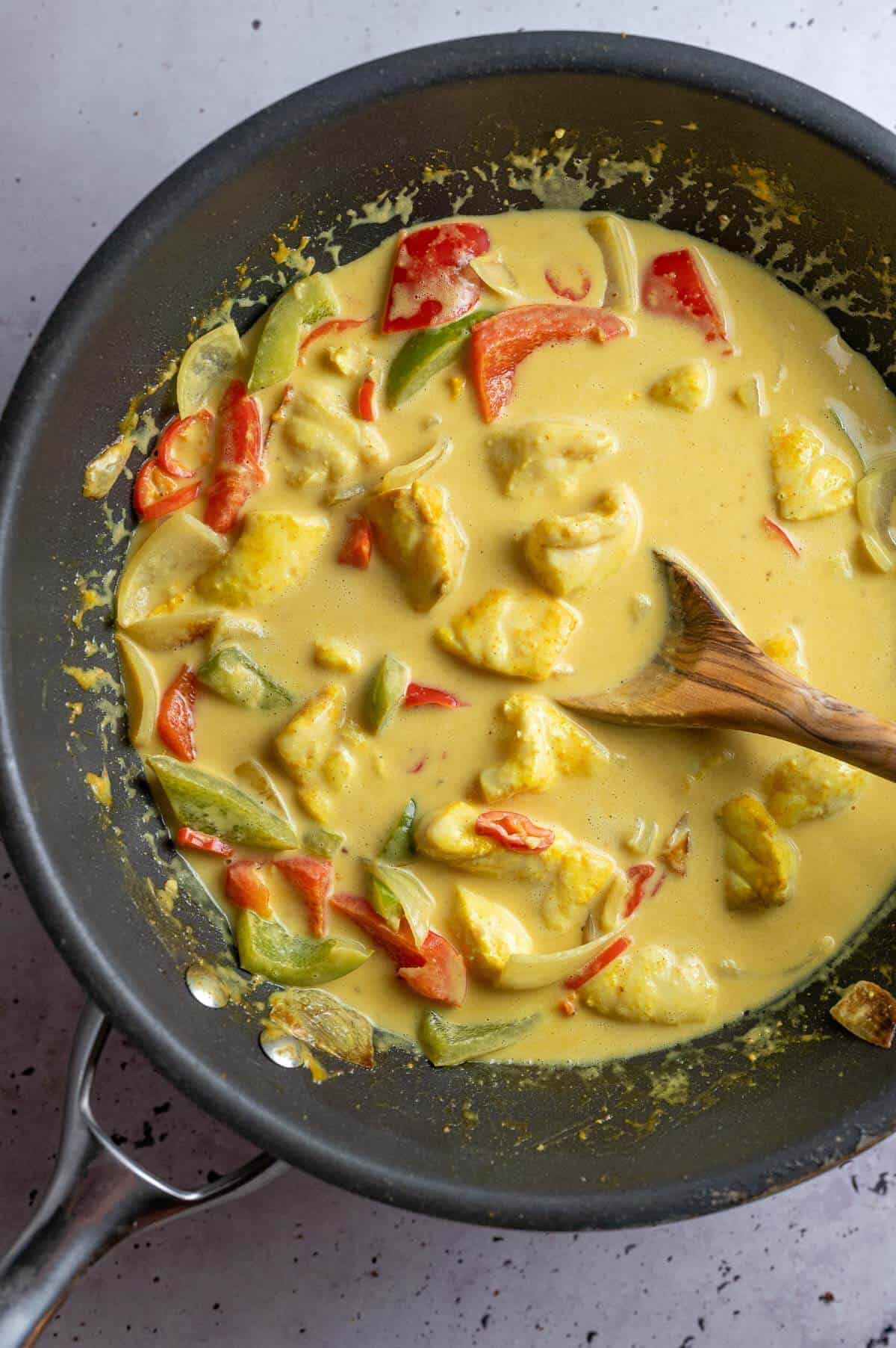 kerala fish curry  in a wok with a wooden spoon