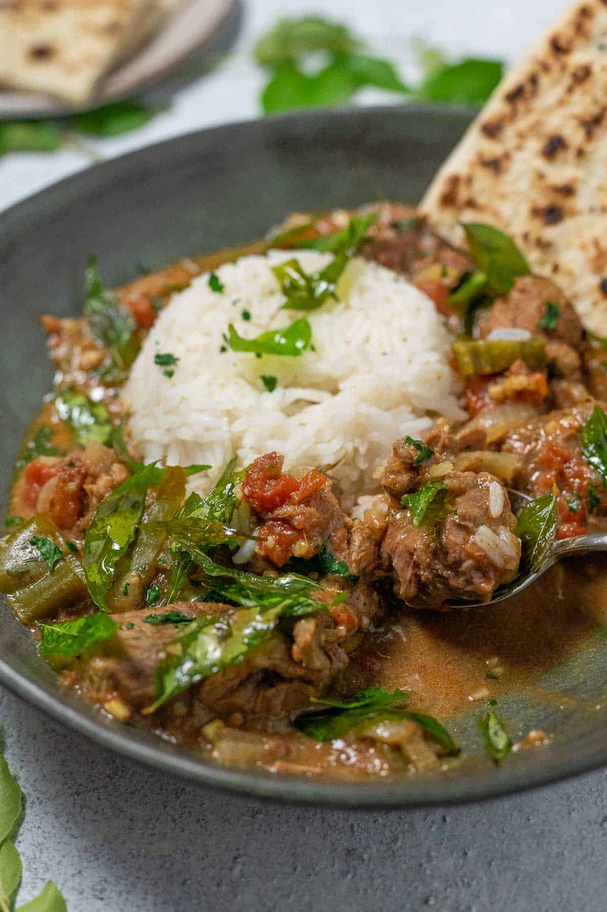 spoon digging into a bowl of indian beef curry with rice and curry leaves
