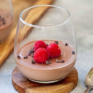 a glass of sugar free panna cotta with raspberries