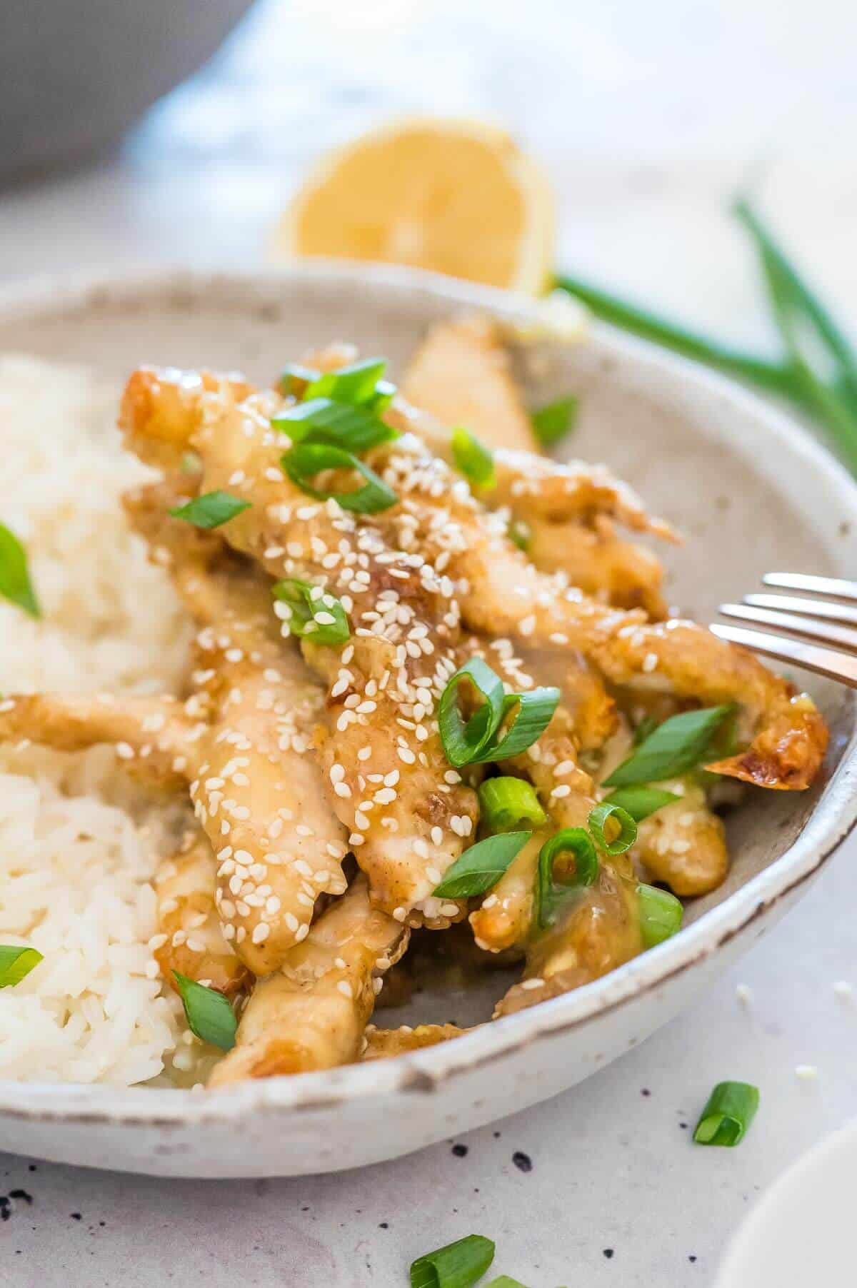 a bowl of honey lemon chicken with a fork in