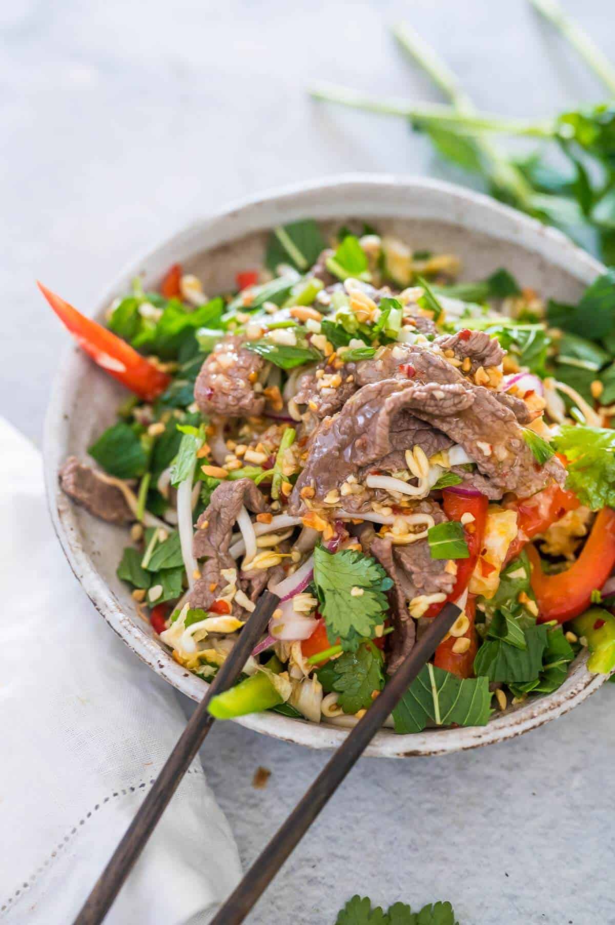 a bowl of vietnamese beef salad with dressing and peanuts on top