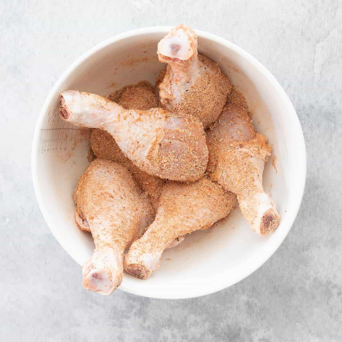 uncooked chicken drumsticks in a bowl with seasoning