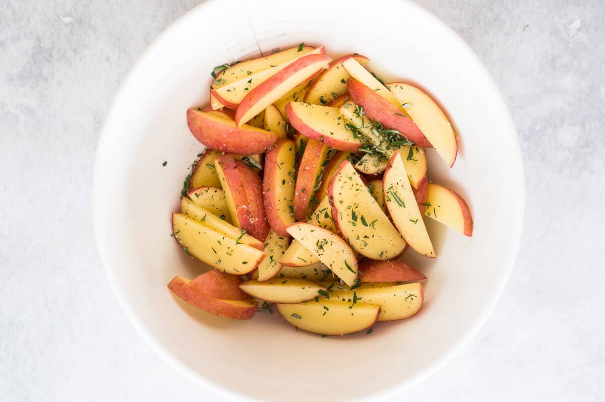 uncooked potato wedges in a white bowl with seasoning