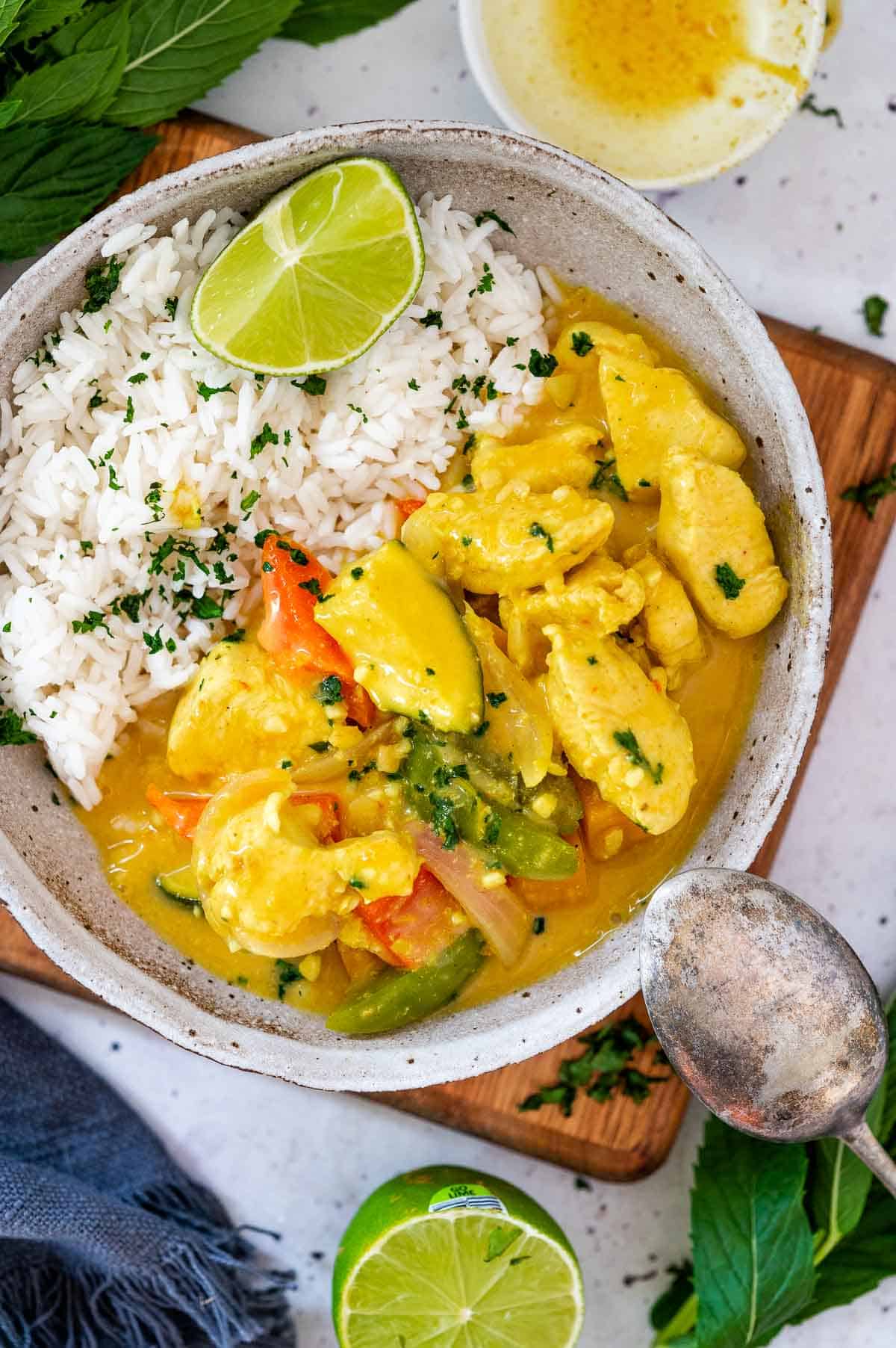 a bowl of creamy chicken curry with rice and lime wedge