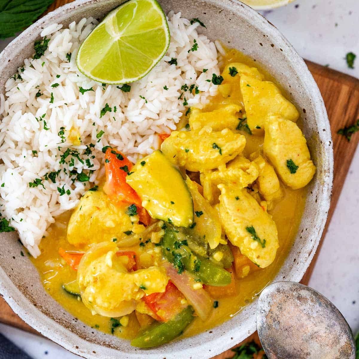 a bowl of thick and creamy yellow coconut chicken curry ready to serve with spoon