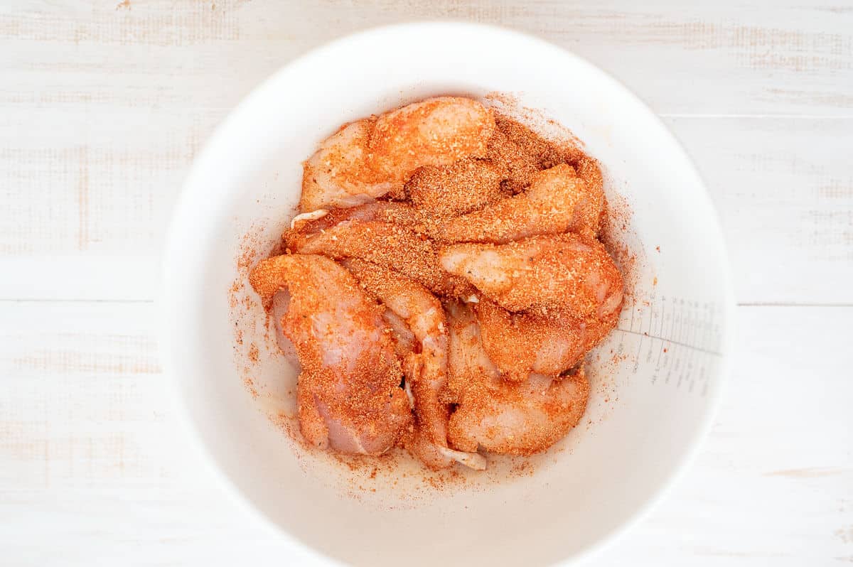 uncoked chicken tenders with seasoning in a white bowl