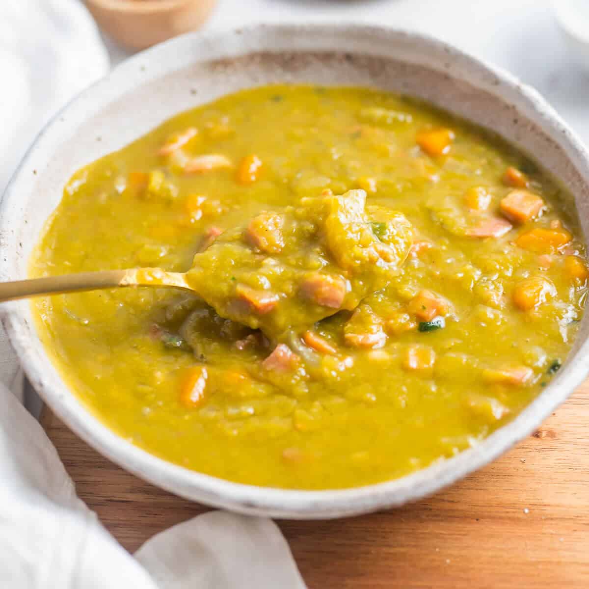 a bowl of split pea soup with bacon with spoon in