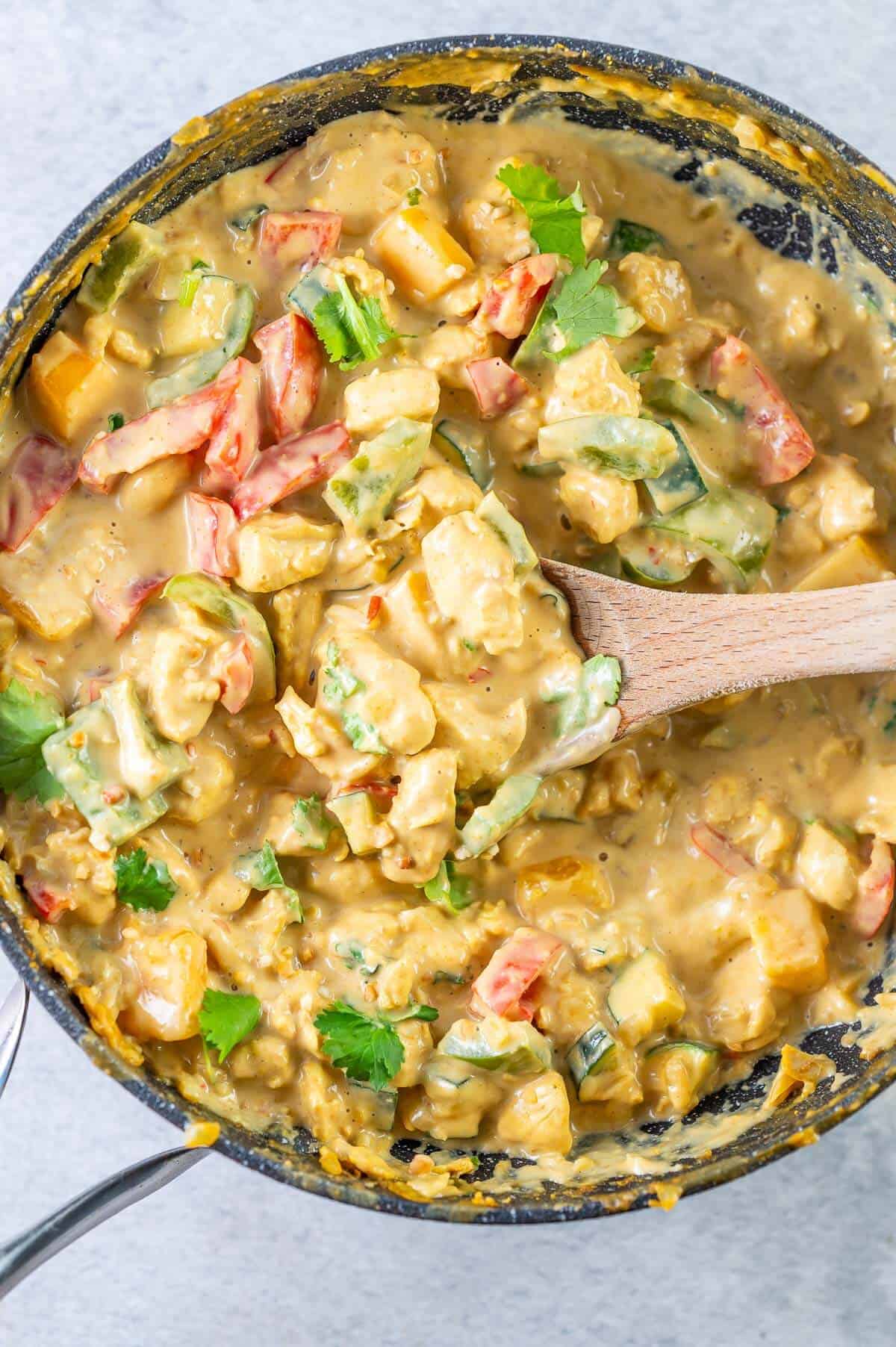 satay chicken and veges in a pan with wooden spoon dipped in