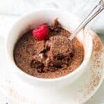 chocolate cake in a mug with one raspberry and a spoon digging in