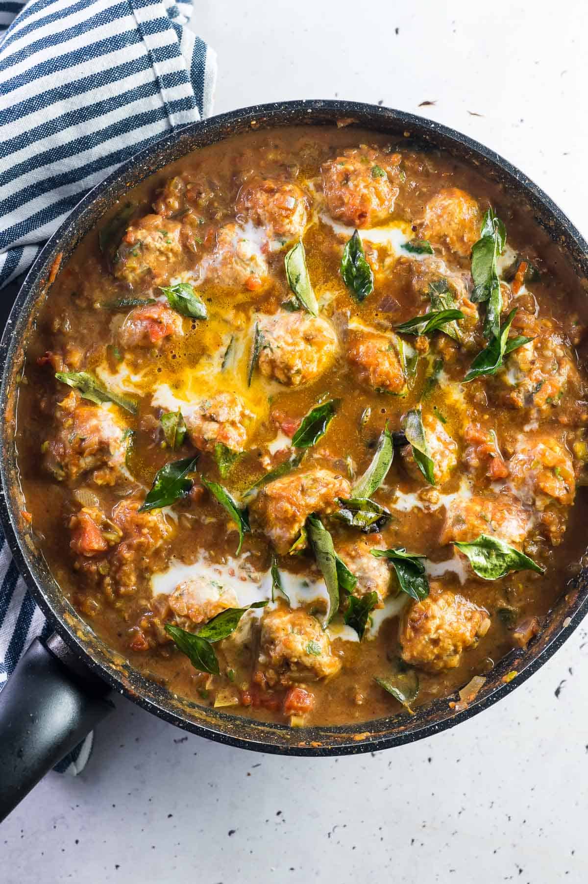 cooked butter chicken meatballs in a pan with curry leaves and coconut milk