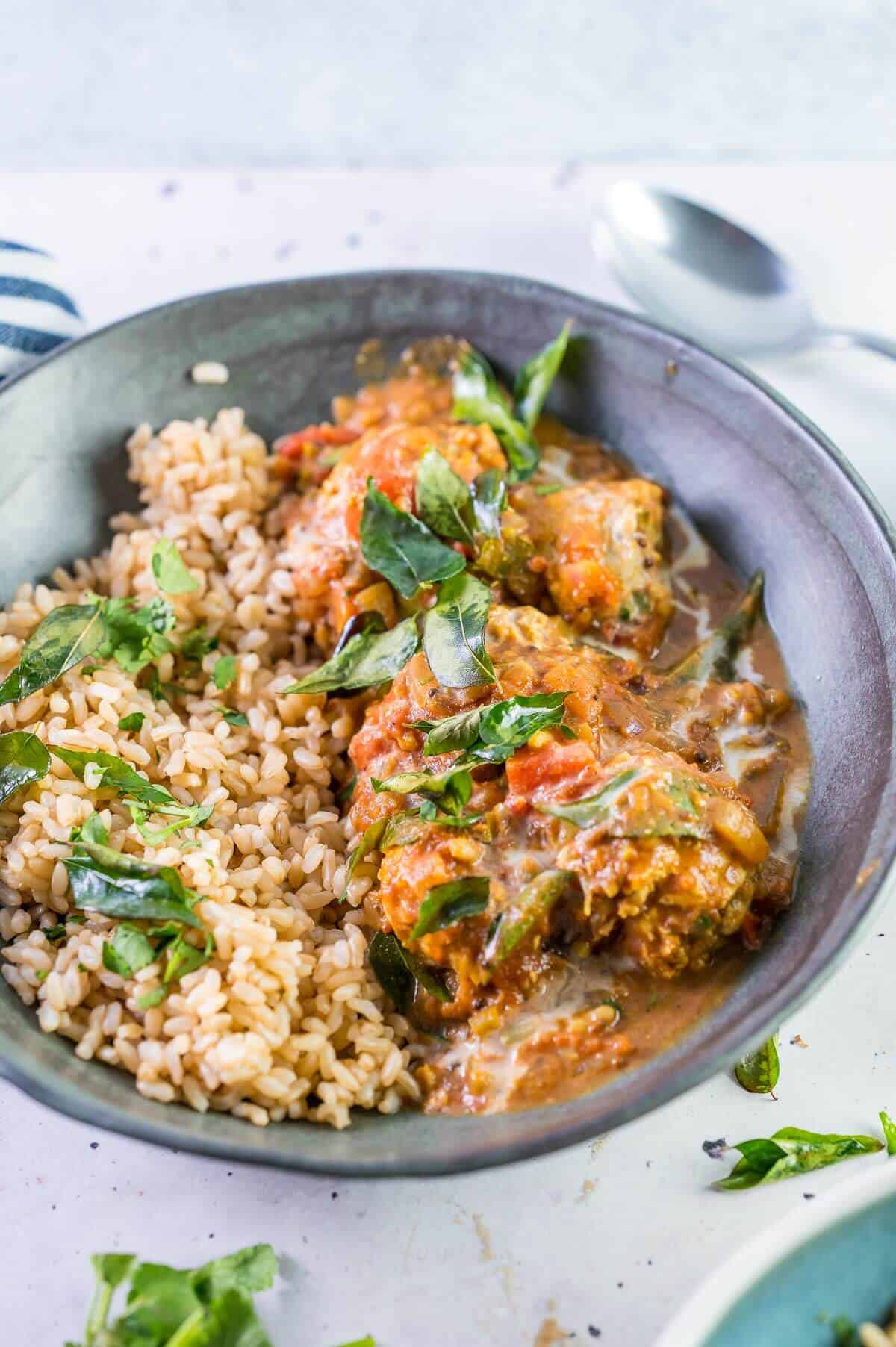 butter chicken meatballs in a bowl with rice and curry leaves on top