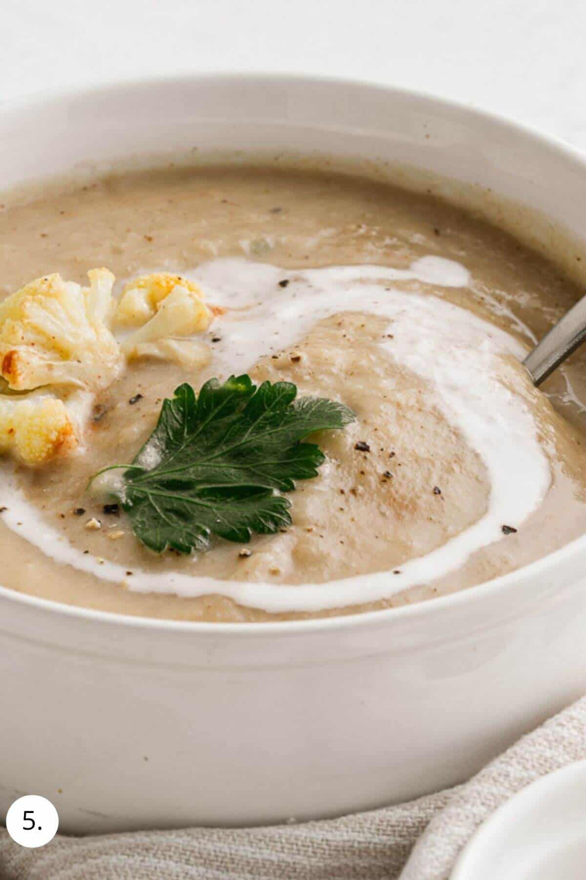 cauliflower soup in a bowl with parsley and ream