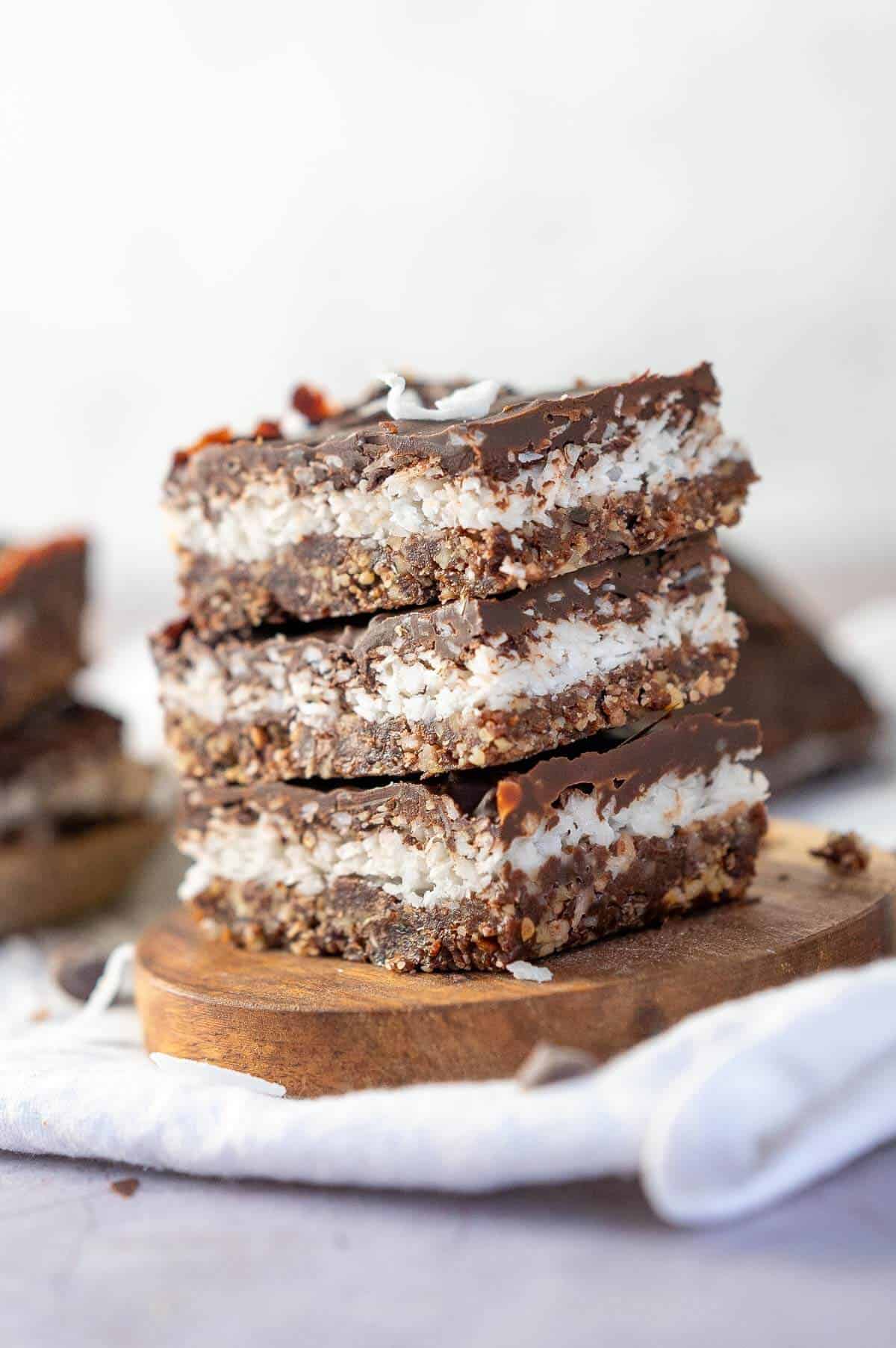 3 chocolate coconut bars stacked on a wooden coaster