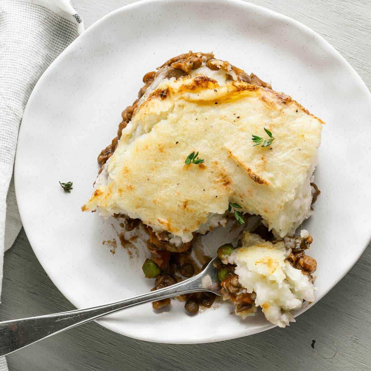 a slice of lentil shepherds pie on a plate with a fork dug in
