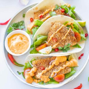 three air fryer fish tacos on a plate with sauce