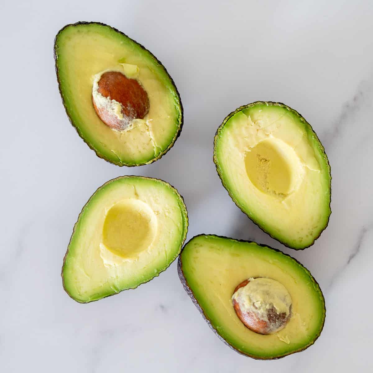 four avocado halves on a bench