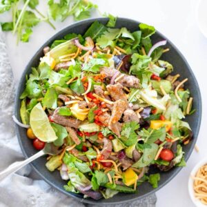 a bowl of thai beef salad with noodles and mango