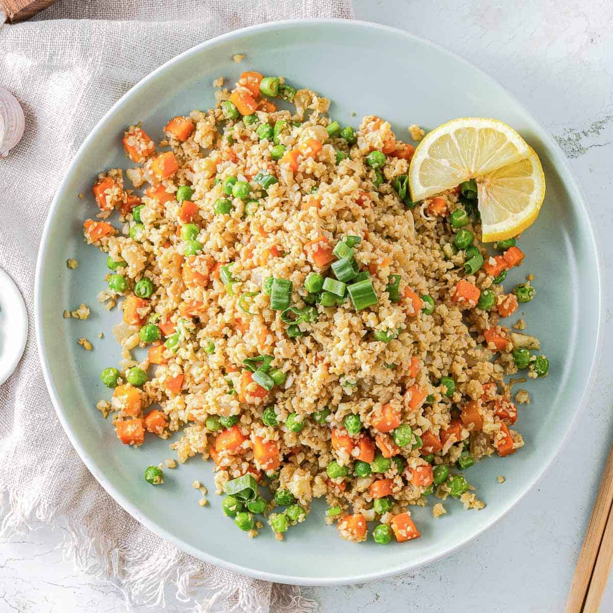 Cauliflower fried rice on a blue plate with lemon wedge