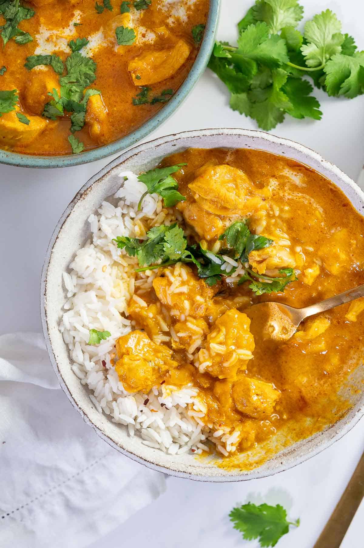 rustic white bowl with mango chicken curry pieces, rice and corriander