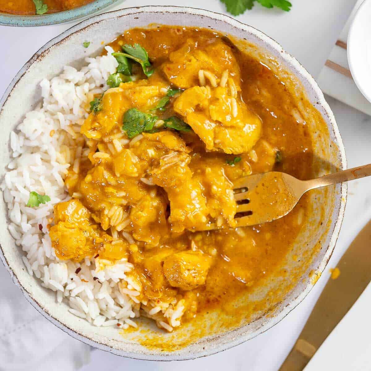 creamy mango chicken curry slow cooked in a bowl with a fork